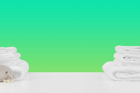 Stacked clean towels on white table against color background
