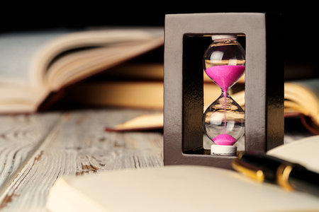 Sandglass on wooden table with opened book close up