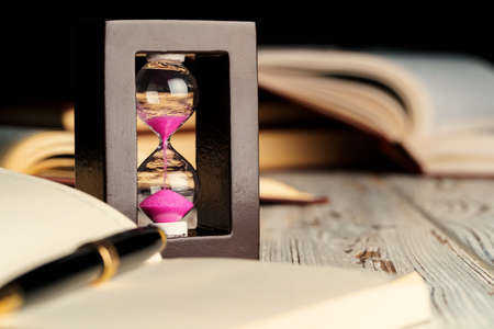 Sandglass on wooden table with opened book close up