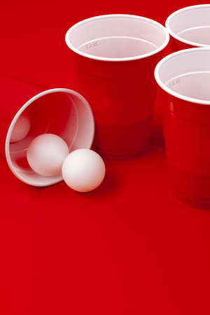 Cups and plastic ball on red background. Beer pong game