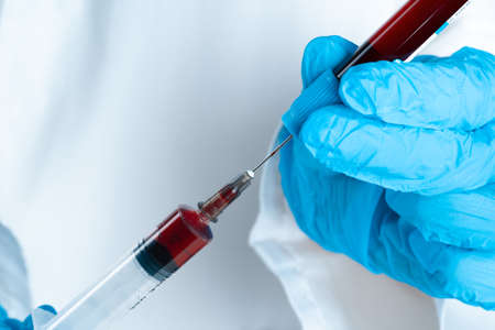 Doctor in blue gloves keep in hands test tube with a blood and syringeの写真素材