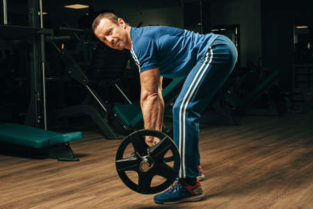Fit elderly man lifting barbell in a gym