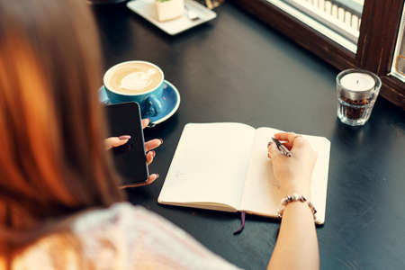 Young business woman sitting at the table in a coffee shop and making notesの写真素材