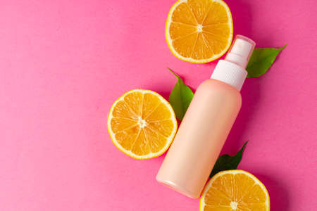 Cosmetic bottle with sliced citrus fruits on bright pink backgroundの写真素材