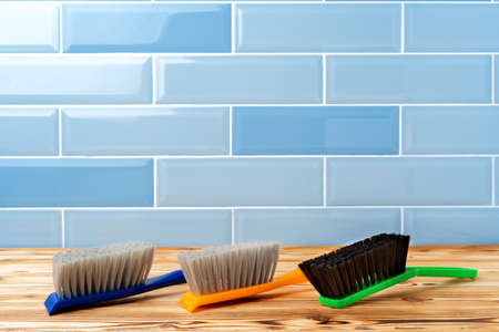 Dust cleaning brushes on wooden table against tile wall