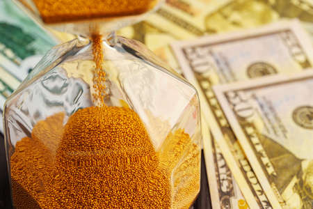Hourglass on stack of dollar banknotes close up