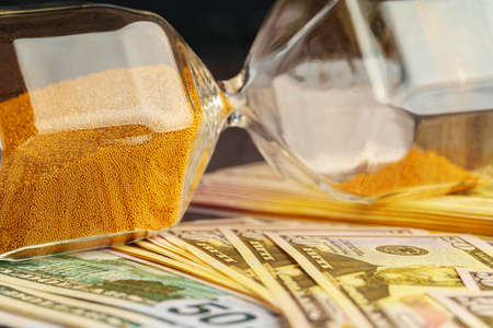 Hourglass on stack of dollar banknotes close up