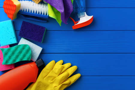 Household cleaning supplies on blue wooden background flat lay