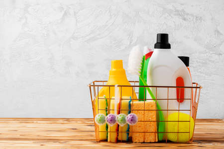 Cleaning tools and chemicals in basket on wooden table against gray backgroundの写真素材