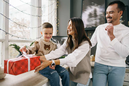 Smiling parents giving Christmas present to son at homeの写真素材