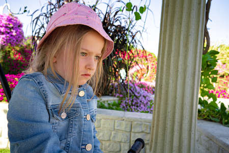 Sad little girl in pink hat sitting in park
