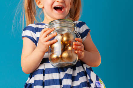 Little cute girl holding glass jar with golden eggs colored for Easterの写真素材