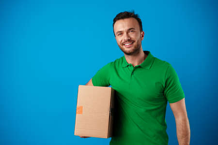 Delivery man with box in studio against blue backgroundの写真素材