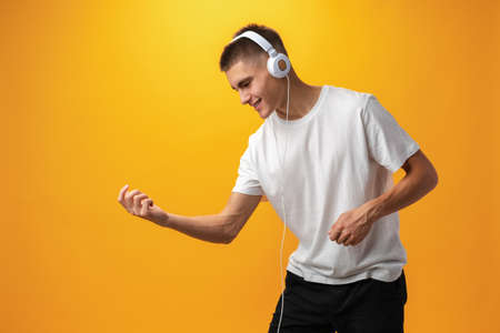 Handsome teenage boy with headphones on head against yellow background