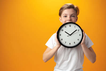 Portrait of a young boy holding a clock against yellow background