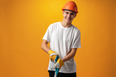 Confident smiling teen boy wearing orange hard hat against yellow backgroundの写真素材
