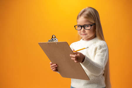 Portrait of little cute girl making notes against yellow backgroundの写真素材