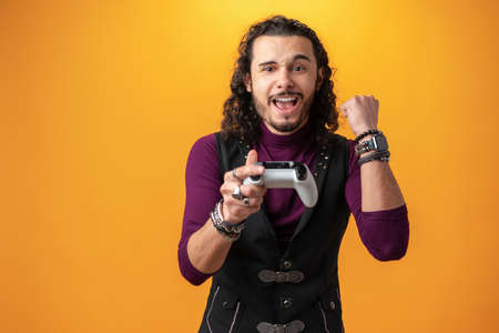 Photo of funny astonished guy with joystick playing video games over yellow background