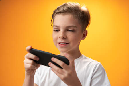 Little kid playing games on smartphone over yellow backgroundの写真素材