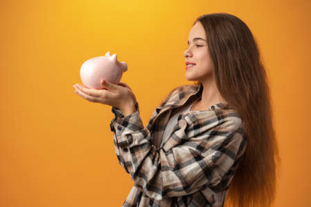 Teen girl with piggy bank on yellow background.の写真素材