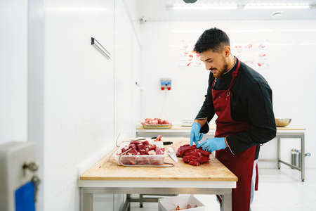 Butcher cutting slices of raw meat on wooden boardの写真素材