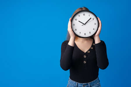 Beautiful teen girl holding wall clock over blue backgroundの写真素材