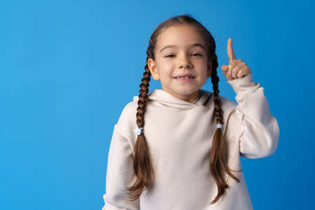 Cute little girl pointing up and having idea against blue background