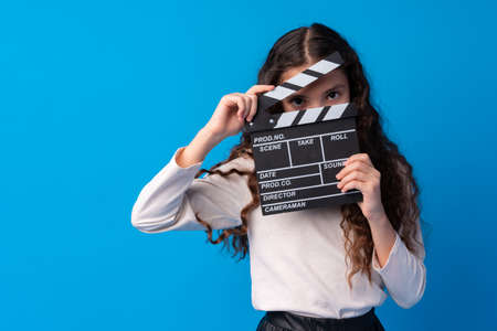 Smiling girl holding clapper board against blue backgroundの写真素材