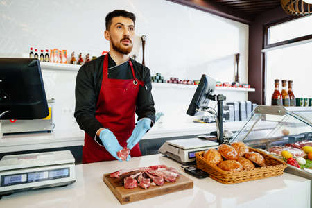 Young butcher holding raw lamb ribs in a butcher shopの写真素材