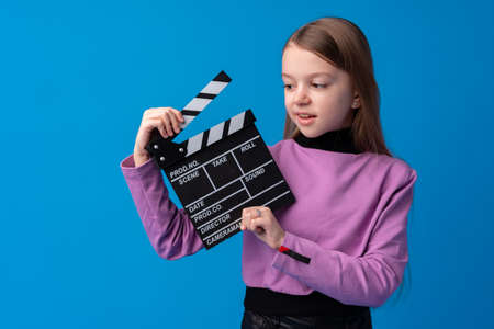 Smiling girl holding clapper board against blue backgroundの写真素材