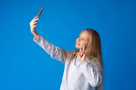 Portrait of an excited little girl taking a selfie isolated over blue backgroundの写真素材