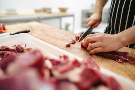 Butcher cutting slices of raw meat on wooden boardの写真素材