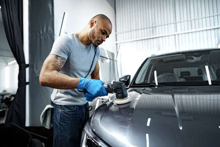 Car detailing. Male hands with orbital polisher in auto repair shop