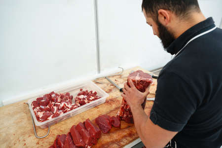 Butcher cutting slices of raw meat on wooden board