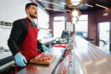 Young butcher holding raw lamb ribs in a butcher shop
