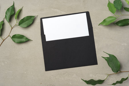 Paper envelope with white blank paper note and plant leaves on tableの写真素材