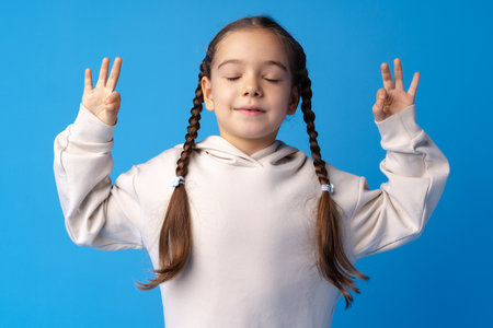 Little girl with braids standing in zen pose against blue backgorundの写真素材