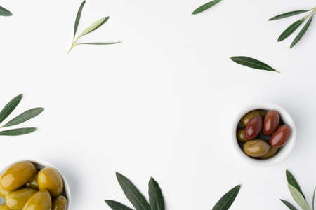 Bowl with green olives and olive leaves on white backgroundの写真素材