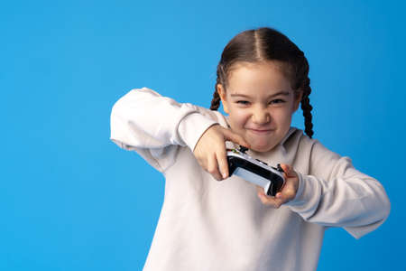Young cute girl plays computer game with joystick on blue backgroundの写真素材