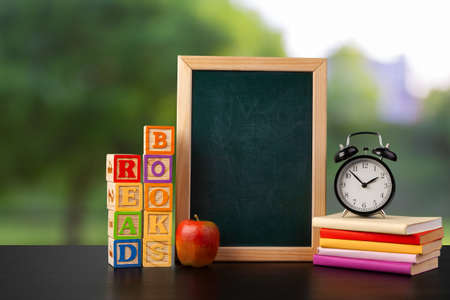 Blackboard and stack of books on wooden table against blurred background