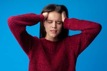 Young woman with headache against blue backgroundの写真素材