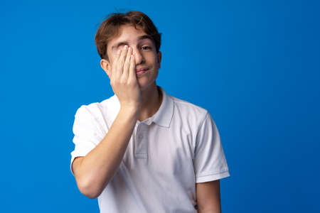 Sad teenager boy failed, touching face against blue backgroundの写真素材
