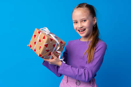 Happy little girl with long hair holding a gift box on a blue background