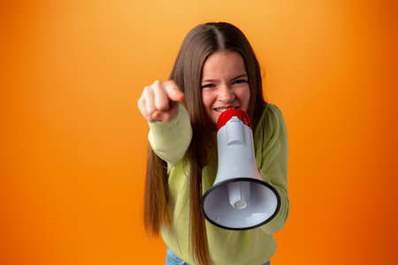 Teen girl making announcement with megaphone against orange backgroundの写真素材