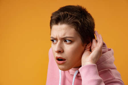 Young girl doing listen gesture with hand on ear over yellow backgroundの写真素材