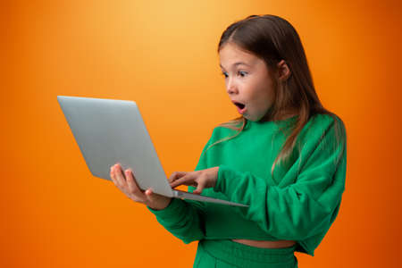 Portrait of a cheerful young teen girl holding laptop computer against orange backgroundの写真素材