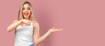 Young smiling woman pointing to copy space isolated on color backgroundの写真素材