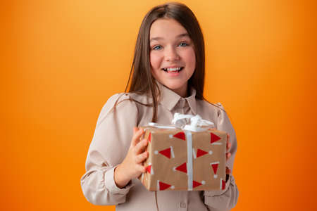 Cute teen girl holding a Christmas gift box against orange background.の写真素材