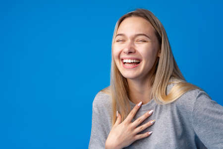 Happy smiling pretty teenage girl laughing over blue backgroundの写真素材