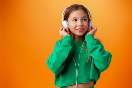 Portrait of modern happy teen school girl with headphones on orange backgroundの写真素材